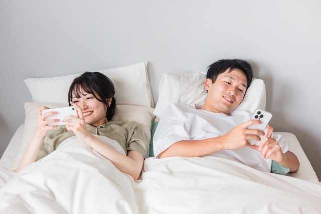 ベットに寝転びながらスマホを見る夫婦
